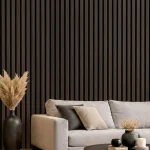 Smoked oak acoustic slat wood panels installed as a feature wall behind a grey sofa in a modern lounge.